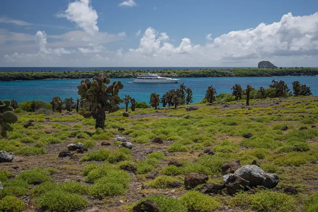 Galápagos coastline with a yacht in turquoise water near volcanic terrain