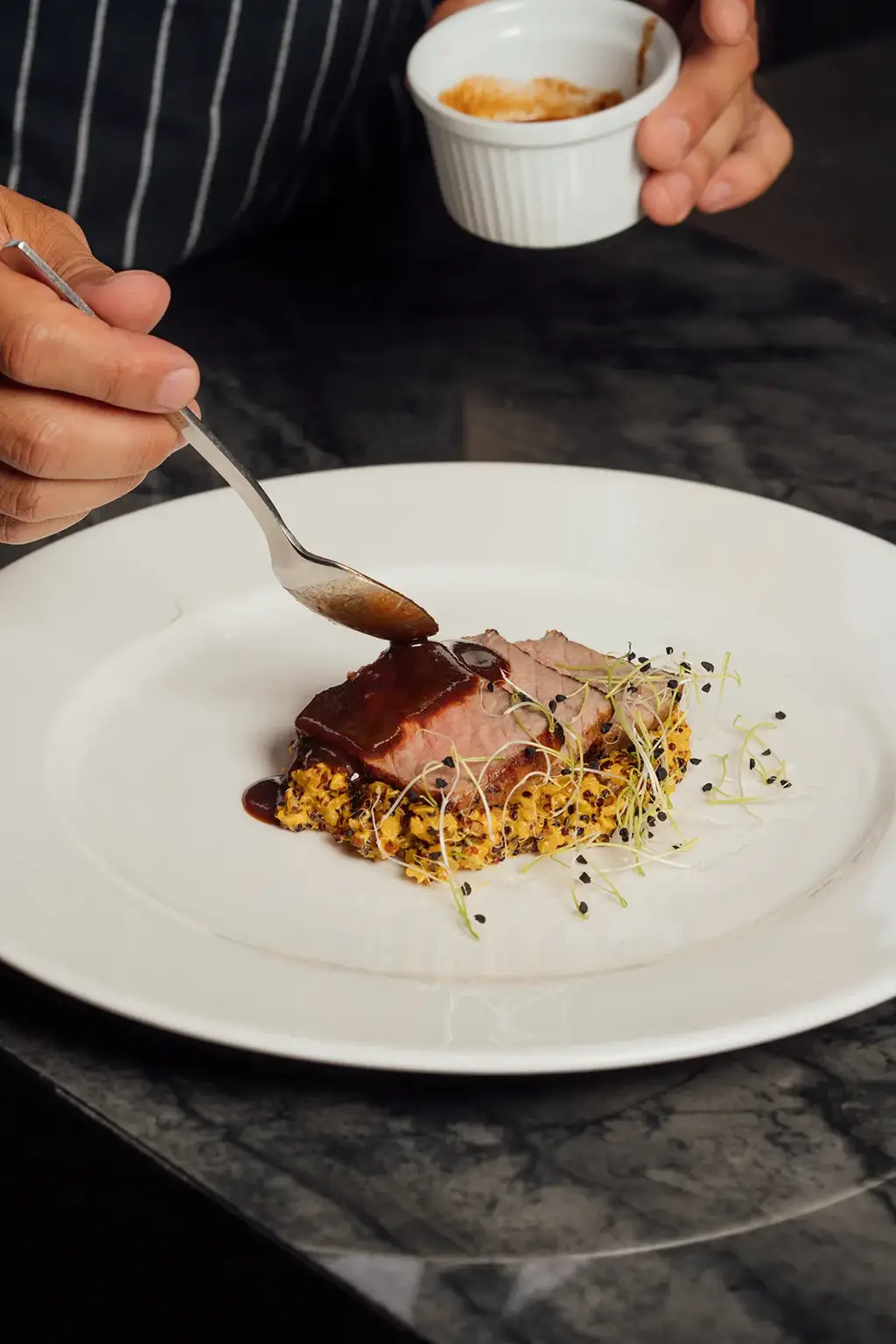 Hands drizzling sauce onto a refined plate